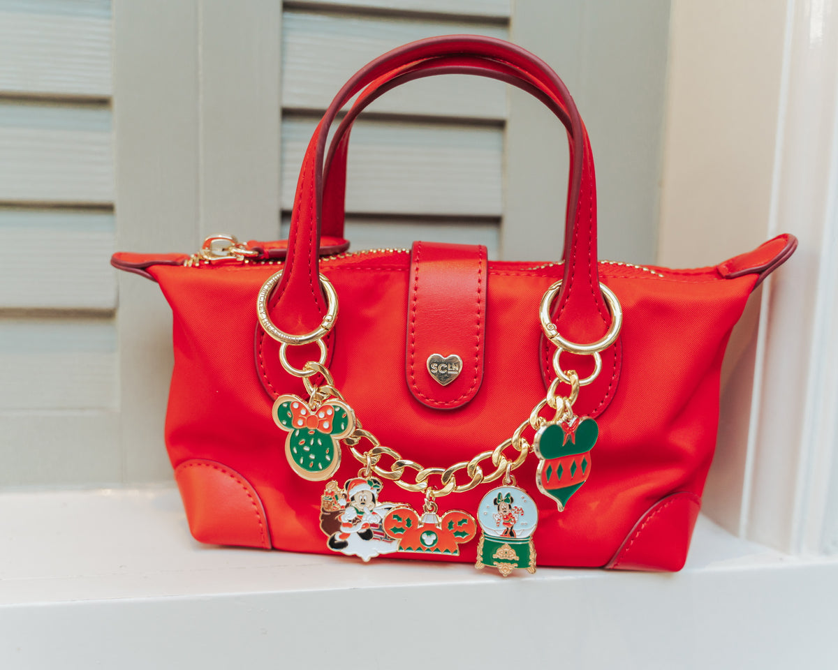 Red handbag with gold chain and character charms on a white surface.
