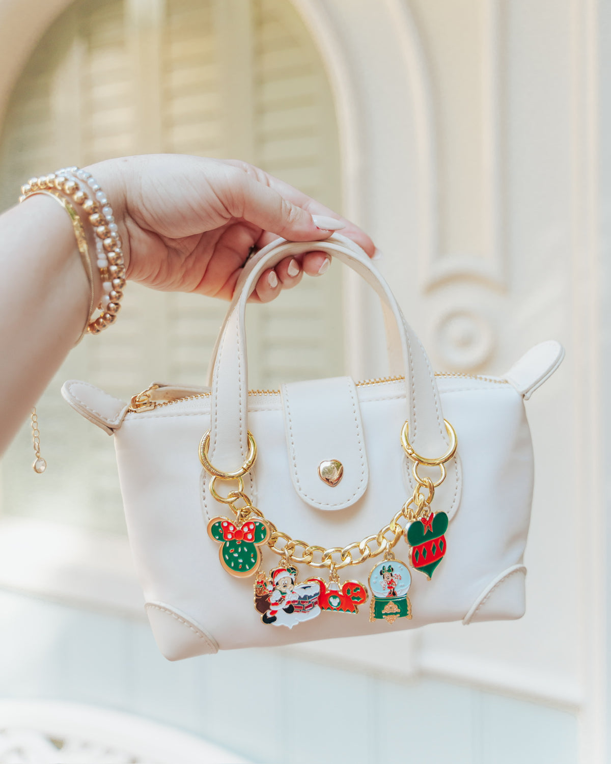 White handbag with decorative charms held by a hand against a neutral background