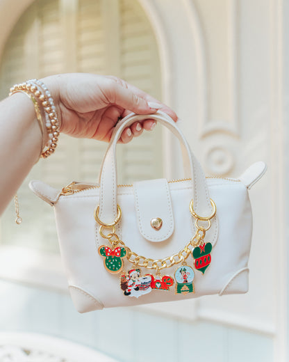 White handbag with decorative charms held by a hand against a neutral background