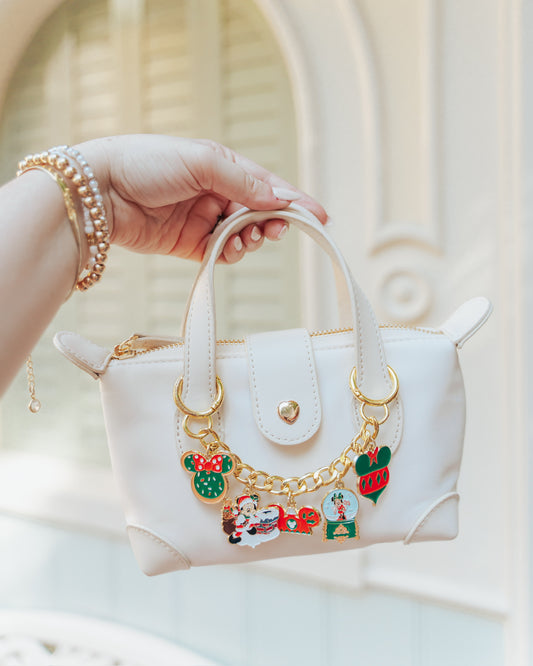 White handbag with decorative charms held by a hand against a neutral background