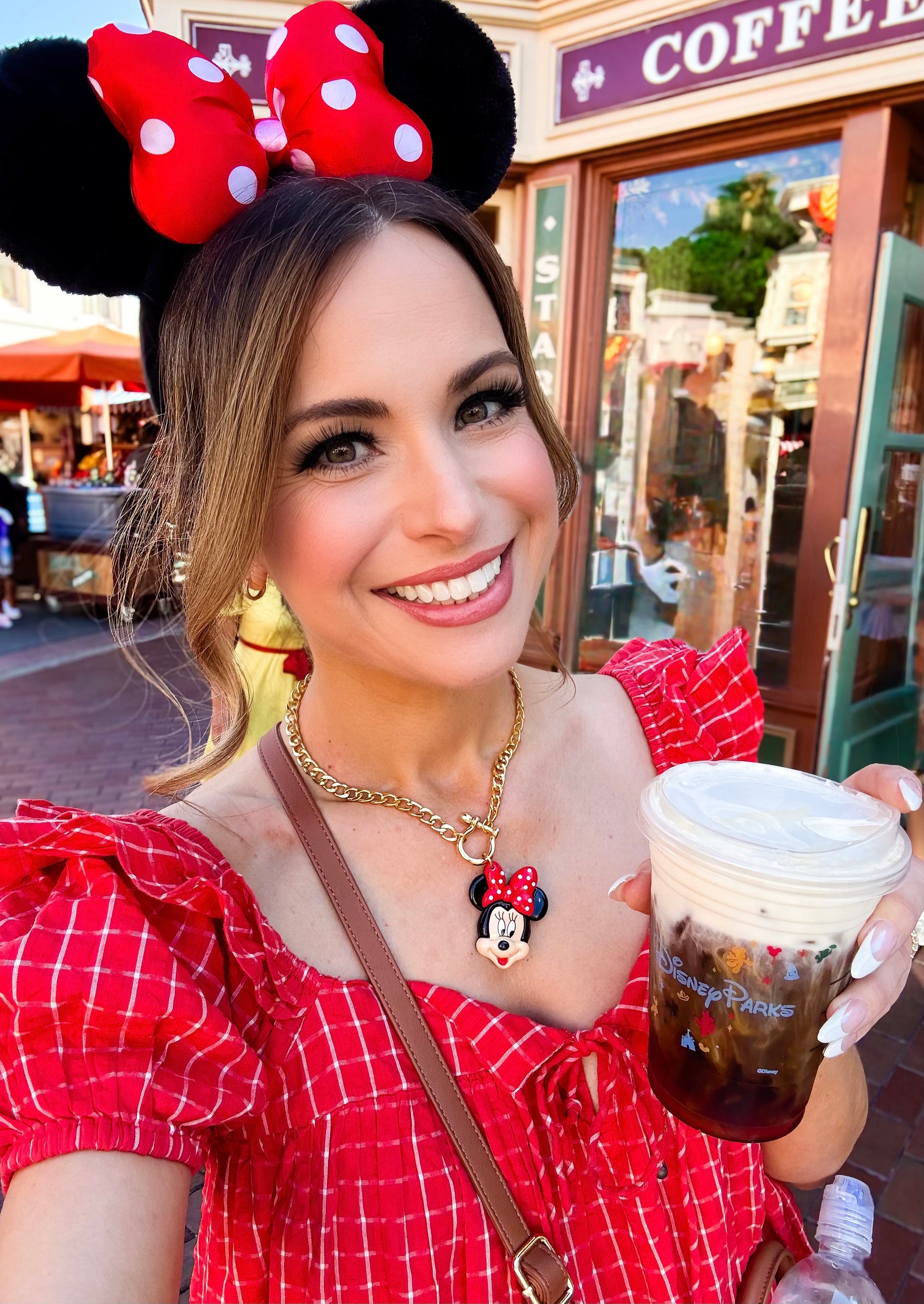 Woman in a red dress and Minnie Mouse ears holding a coffee cup in front of a Disney store.